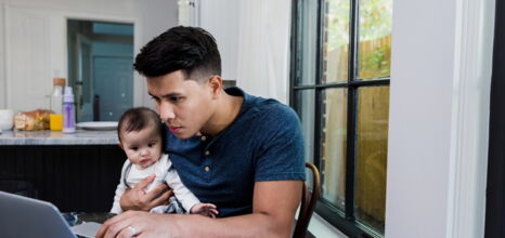 Mann arbeitet am Laptop mit Baby auf dem Schoss