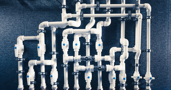 Weiße Kunststoffrohre und Ventile in komplexem Leitungssystem vor dunkler Wand