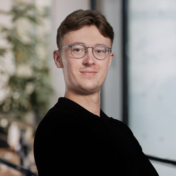 Junger Mann mit Brille und schwarzem Pullover lächelt