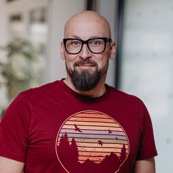 Mann mit Bart und Brille im roten T-Shirt mit Sonnenuntergangs-Motiv