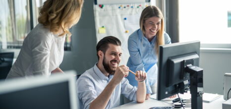 Eine Gruppe lachender Menschen die vor einem Computer sitzen