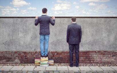 Zwei Männer vor einer Mauer, einer auf Büchern stehend, symbolisiert Wissensvorsprung.