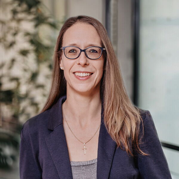 Frau mit Brille und Kreuzanhänger im Business-Outfit vor einem hellen Hintergrund