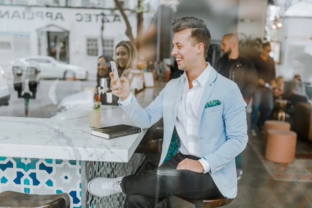Lächelnder Mann in einer Bar mit Handy in der Hand