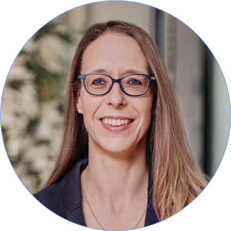 Frau mit Brille und Kreuzanhänger im Business-Outfit vor einem hellen Hintergrund